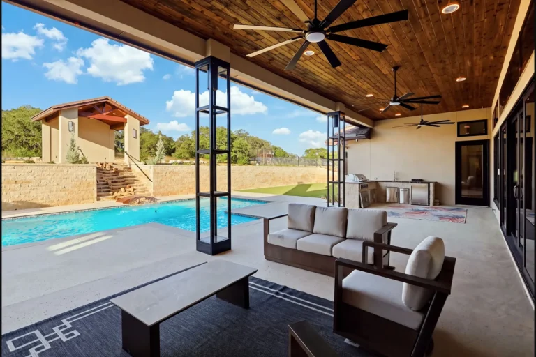Covered patio with a cedar ceiling, outdoor kitchen and lounge seating overlooking the pool and cabana in Boerne, TX