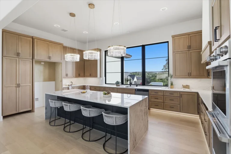 Kitchen with white oak cabinetry, a quartzite waterfall island, crystal pendants and under-cabinet lighting in a Boerne custom home