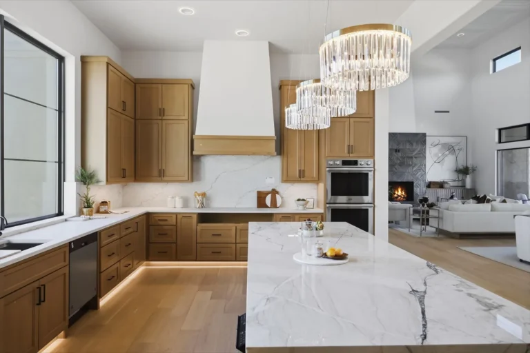 Kitchen with a quartzite island, plaster range hood and double wall ovens open to the living room fireplace in Boerne, TX