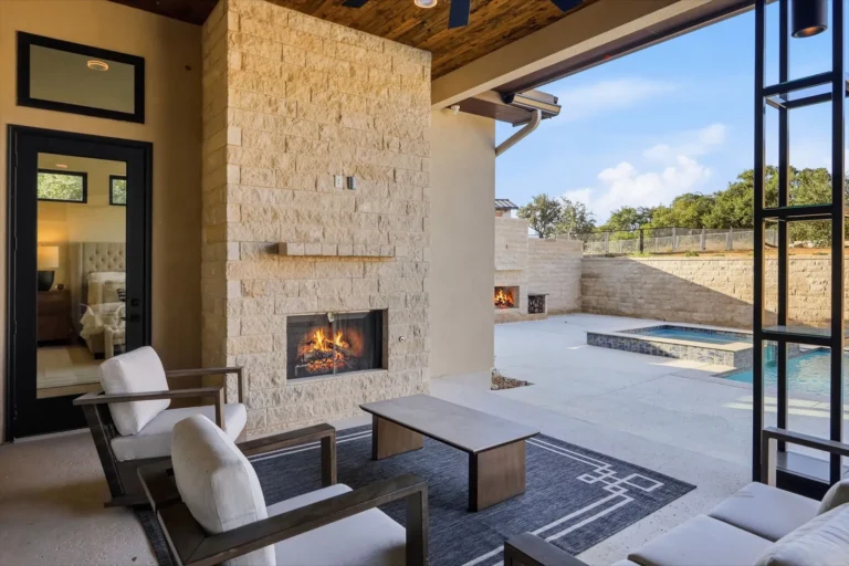 Covered outdoor living room with a limestone fireplace, cedar ceiling and pool view in Boerne, TX