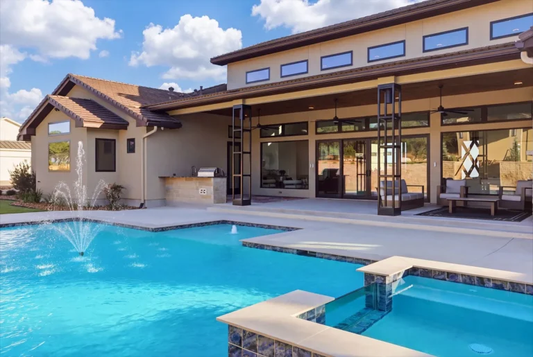 Pool fountains in front of a covered patio with steel columns and an outdoor kitchen in Boerne, TX