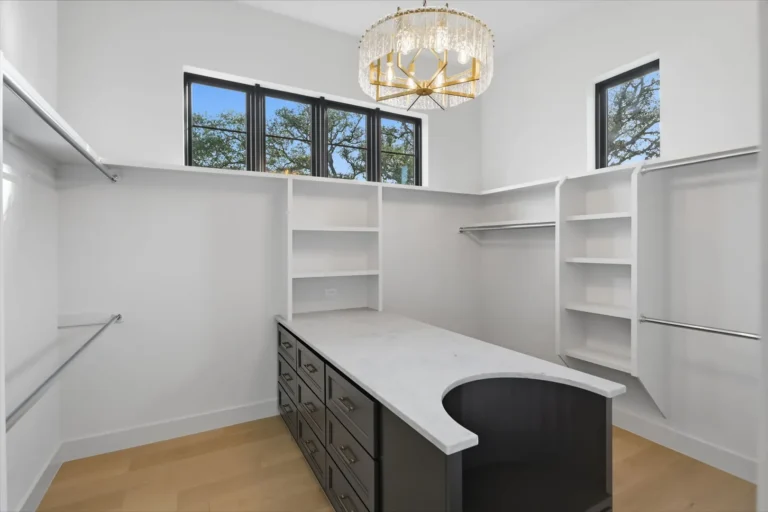 Walk-in closet with custom shelving, hanging rods, a crystal chandelier and center island in a Boerne, TX custom home