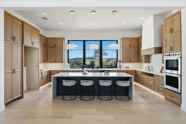 White oak kitchen with a navy waterfall island, crystal pendant lights and a window wall overlooking the hills in Boerne, TX