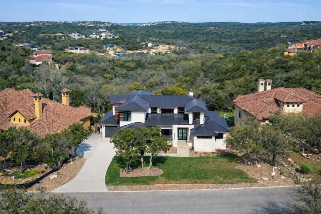 Aerial view of a two-story contemporary custom home with a dark metal roof set against the wooded Texas Hill Country