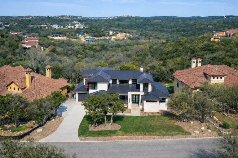Aerial view of a two-story contemporary custom home with a dark metal roof set against the wooded Texas Hill Country