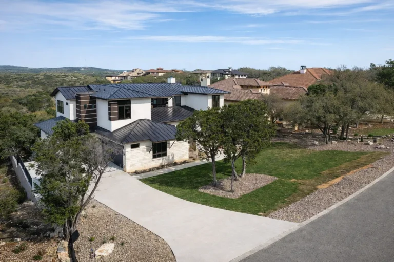Elevated view of a two-story contemporary custom home with dark metal roofs among live oaks and rolling Texas Hill Country views
