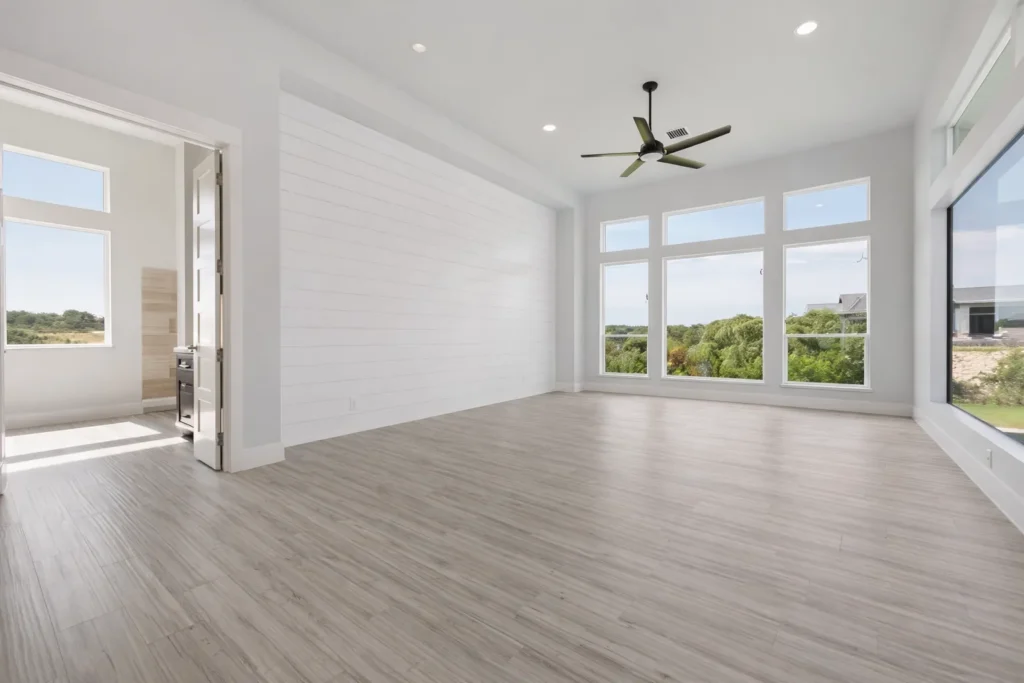 Bright flex room with a shiplap accent wall, black ceiling fan, tall windows and wood-look tile floors framing Hill Country views