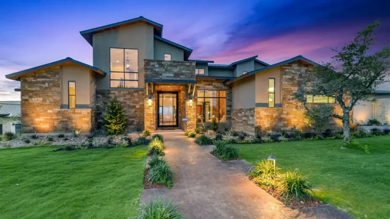 Contemporary stone and stucco custom home with a shed roofline, lit entry and landscaped walkway at twilight