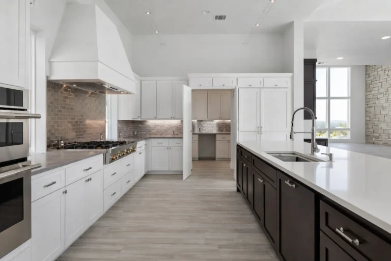 White chef's kitchen with a tall range hood, professional range, butler's pantry and a dark island with quartz counters