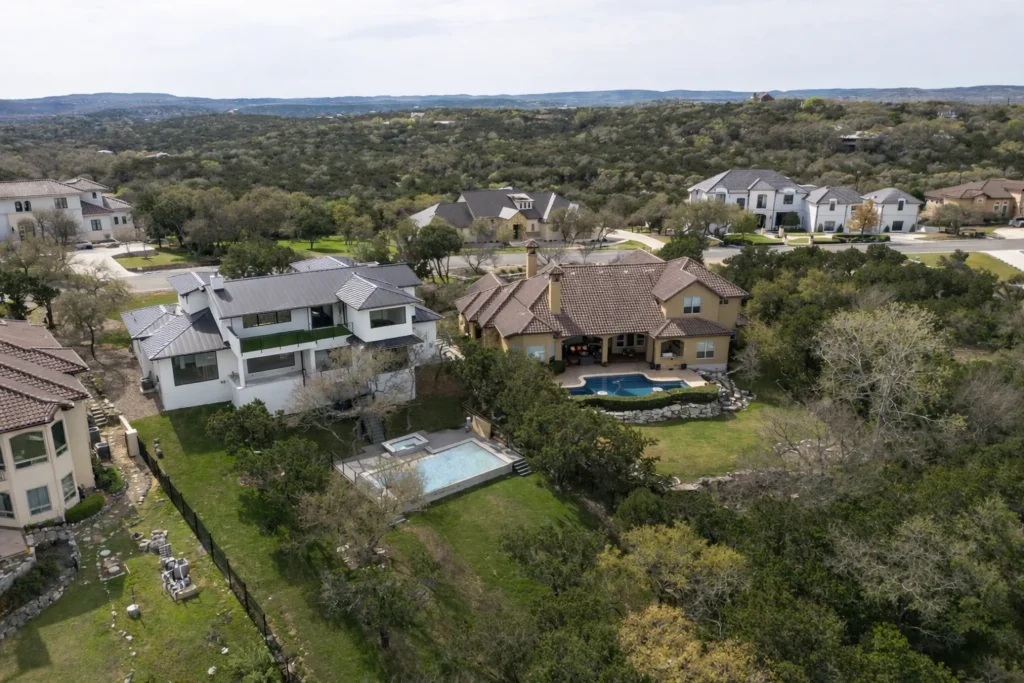 Aerial view of a two-story custom home with a backyard pool overlooking wooded Texas Hill Country