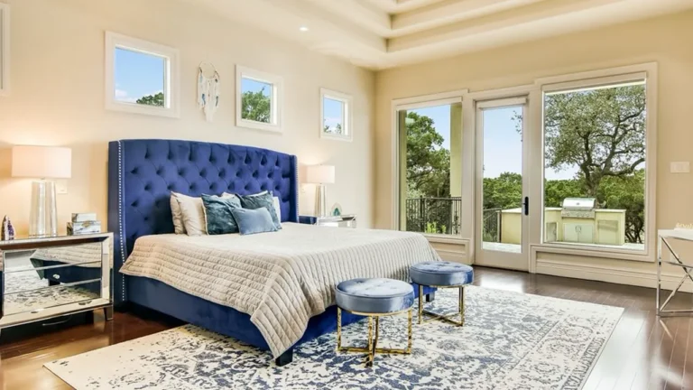 Bedroom with a navy tufted headboard, upholstered stools and glass doors to a balcony with an outdoor kitchen