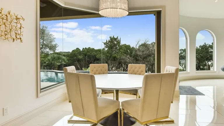 Breakfast nook with a round table, upholstered chairs and a crystal pendant before a picture window overlooking the pool and Hill Country