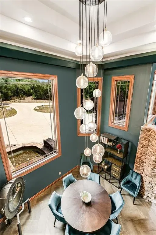 Dining room with deep teal walls, a cascading glass globe chandelier, round table and stacked-stone arches