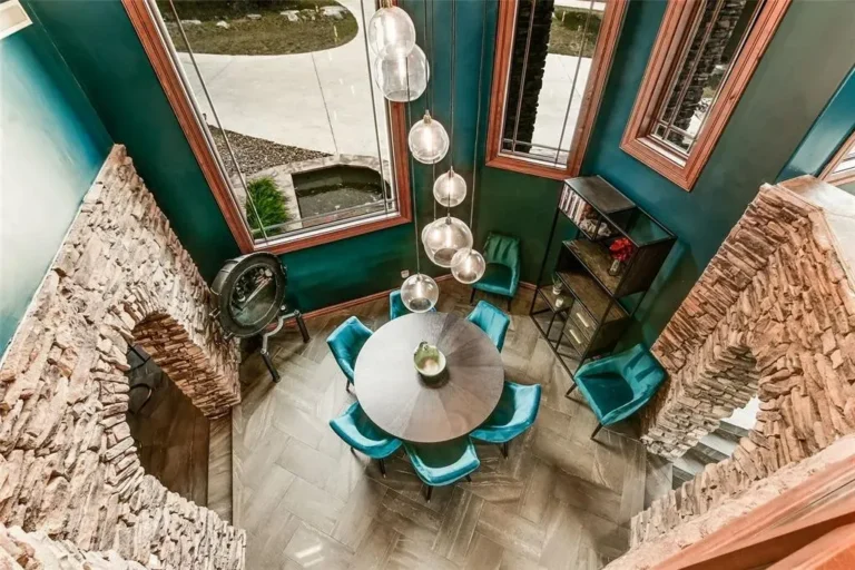Overhead view of a round dining table and teal velvet chairs framed by stacked-stone arches and herringbone floors