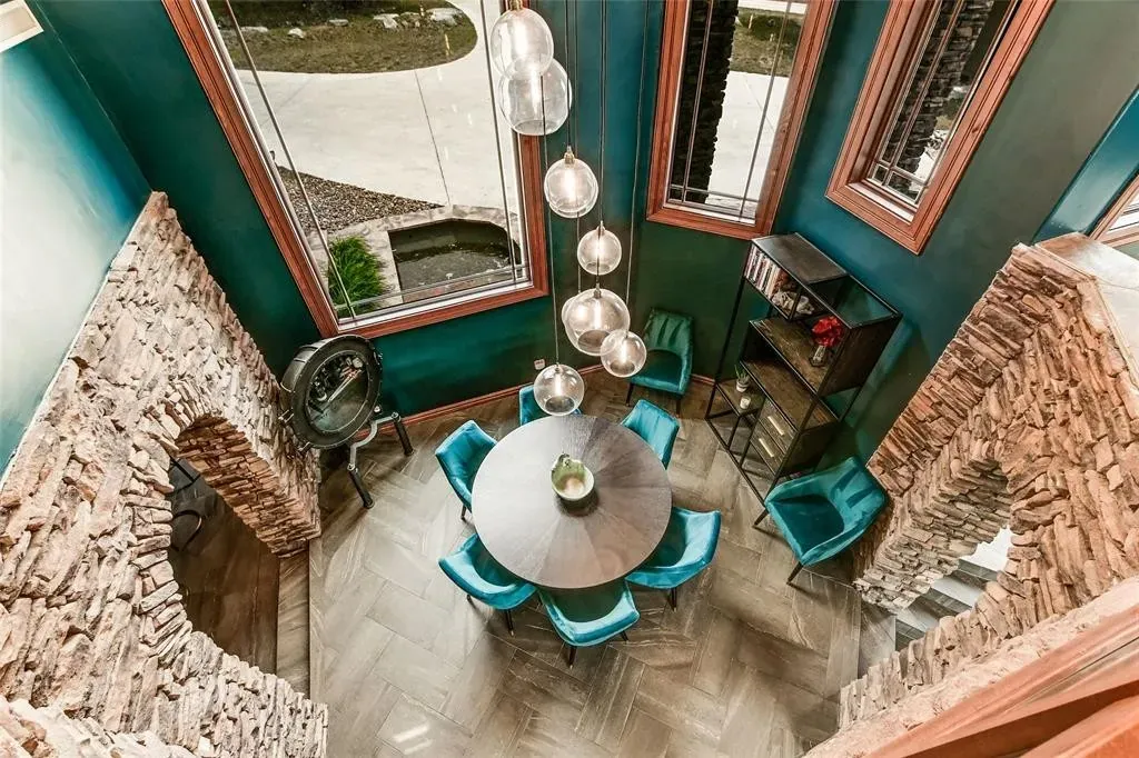 Overhead view of a round dining table and teal velvet chairs framed by stacked-stone arches and herringbone floors