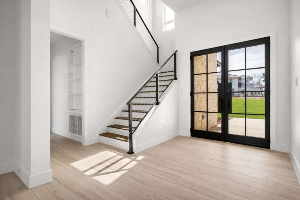 Entry foyer with black steel-and-glass double doors and a floating staircase with a metal railing