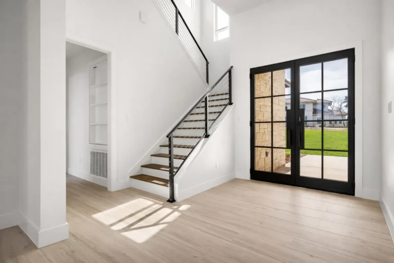 Entry foyer with black steel-and-glass double doors and a floating staircase with a metal railing