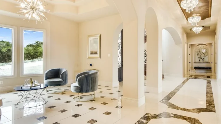 Foyer with polished marble floors and dark inlays, a starburst chandelier, arched openings and a sitting area by the front windows