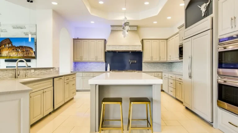 Kitchen with painted cabinetry, a cobalt blue backsplash, gold-base island stools, paneled refrigerator and stacked wall ovens