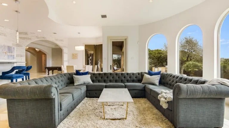 Living room with a U-shaped gray tufted sectional, marble coffee table and arched windows looking out to the trees