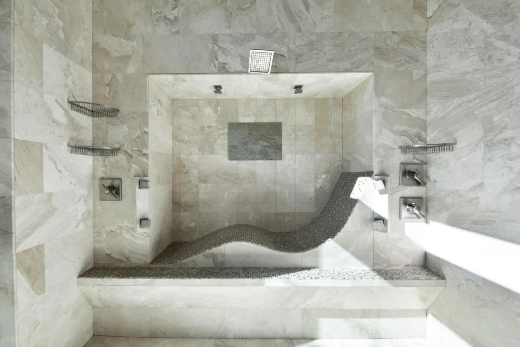 Walk-in marble shower with a sculpted chaise lounge bench, rain shower head and built-in niches