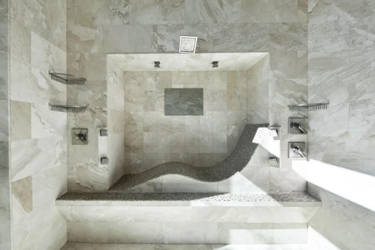 Walk-in marble shower with a sculpted chaise lounge bench, rain shower head and built-in niches