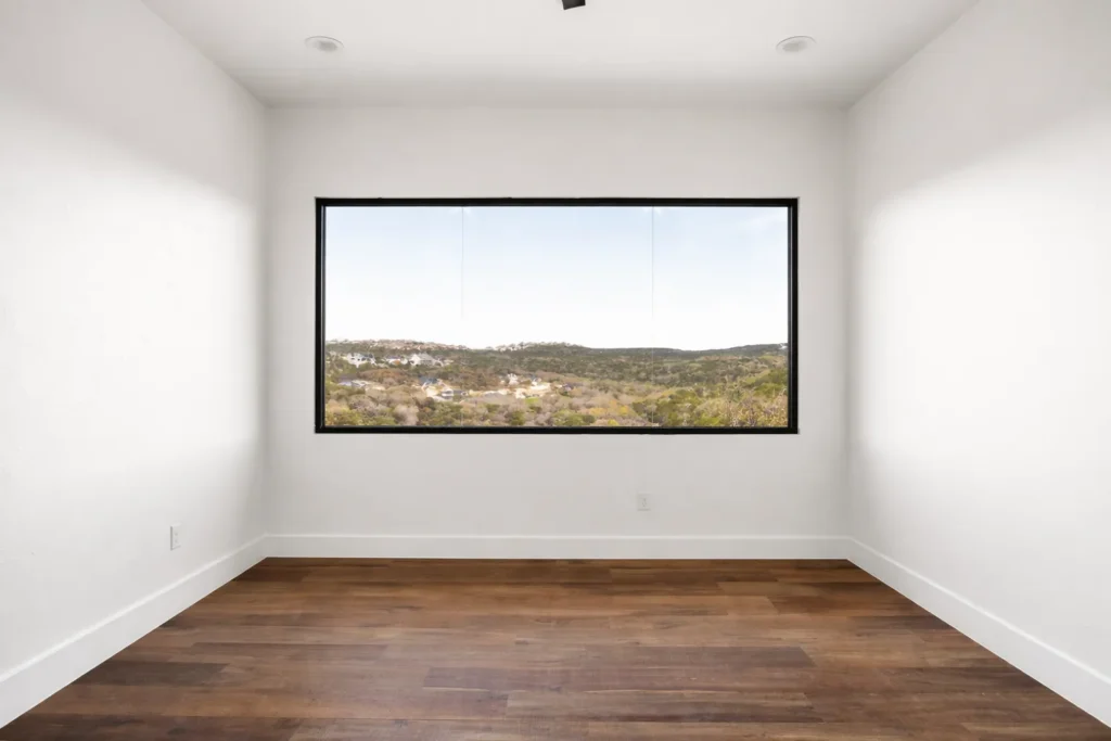 Room with a black-framed picture window framing a sweeping Texas Hill Country view above hardwood floors