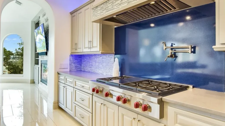 Professional gas range with red knobs, a stainless hood and pot filler set against a sparkling blue quartz backsplash