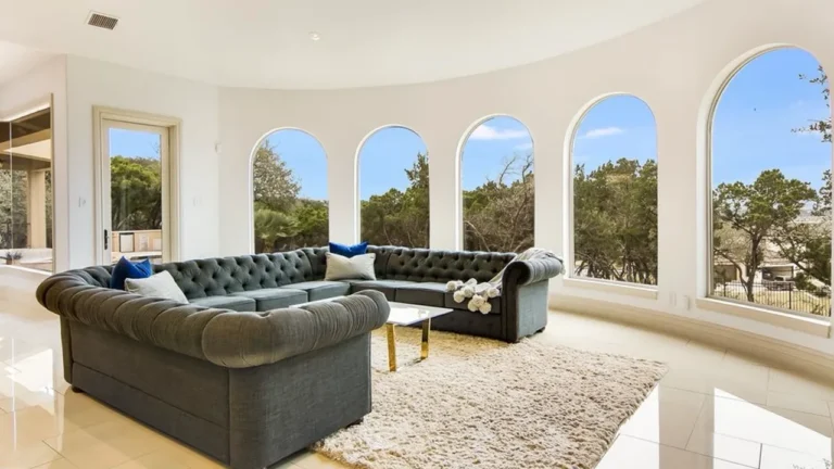 Rounded living room lined with arched windows and a tufted gray sectional overlooking the Hill Country