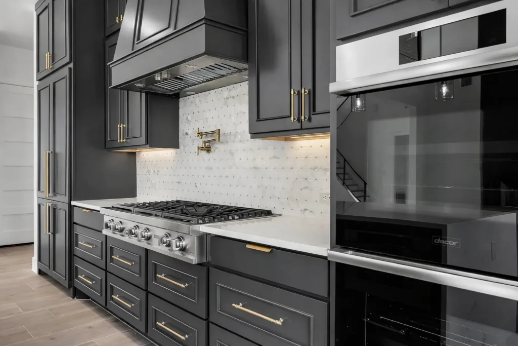 Charcoal shaker cabinets with brass hardware, a professional gas range with pot filler, marble mosaic backsplash and wall ovens