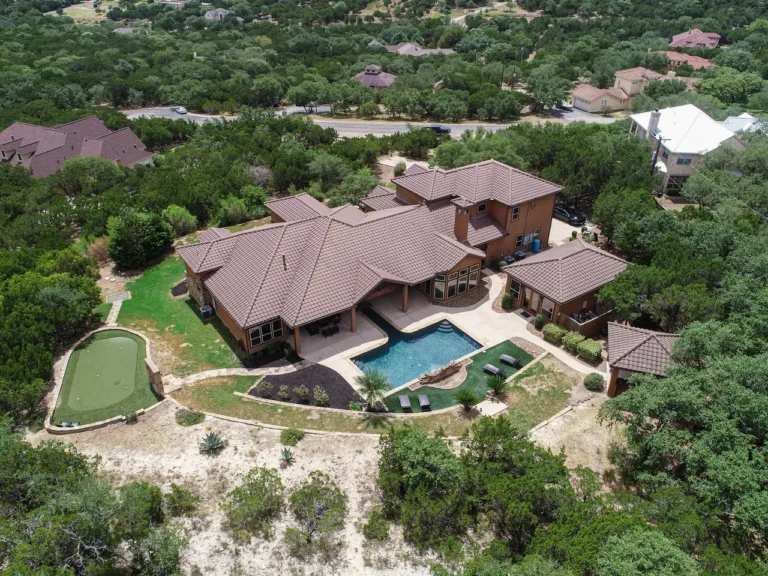 Aerial view of a Hill Country estate with a pool, putting green, casitas and live oak canopy