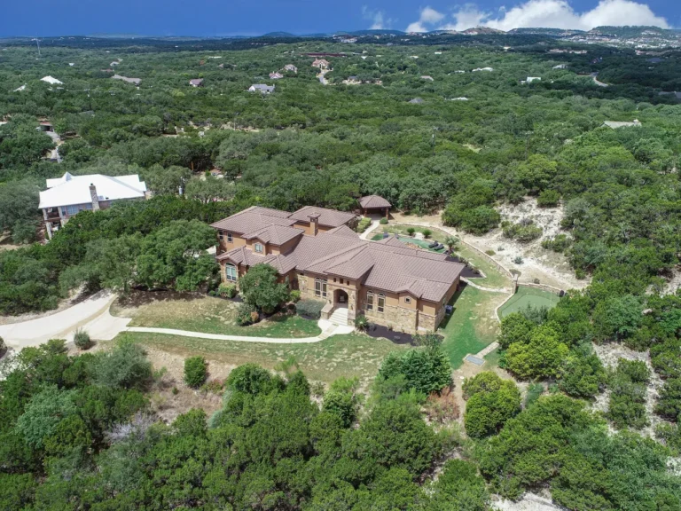 Aerial view of a custom estate home on wooded Texas Hill Country acreage with distant hills