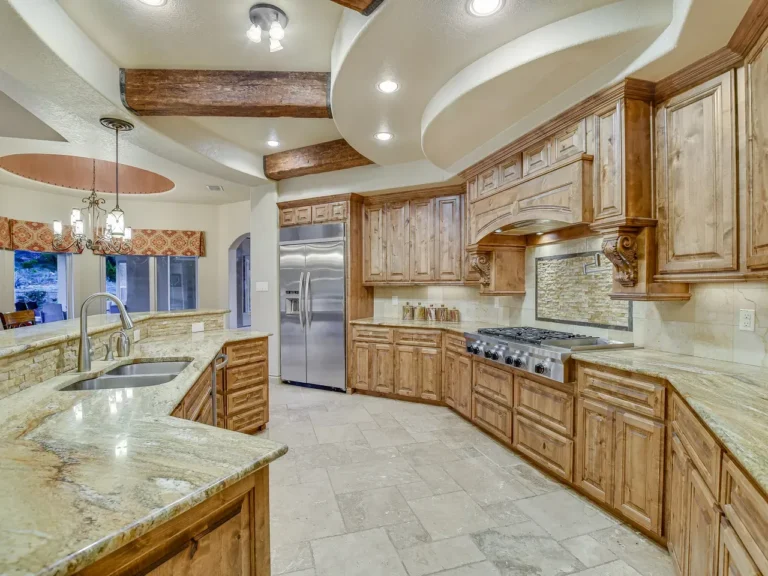 Kitchen with knotty alder cabinetry, granite counters, travertine floors, wood beams and a curved soffit ceiling