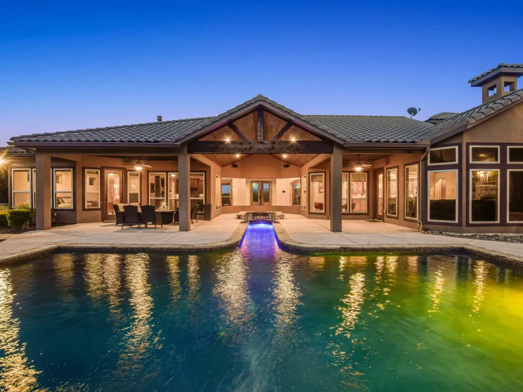 Twilight view across a lit pool to a covered patio with timber trusses at a Texas Hill Country estate home