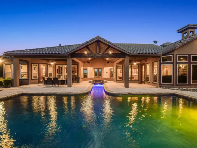 Twilight view across a lit pool to a covered patio with timber trusses at a Texas Hill Country estate home