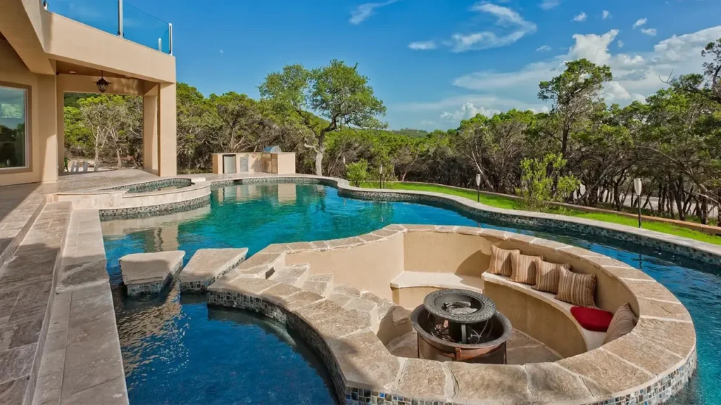Freeform pool with stepping-stone pads and a sunken fire pit lounge with curved built-in seating, set against Hill Country woods