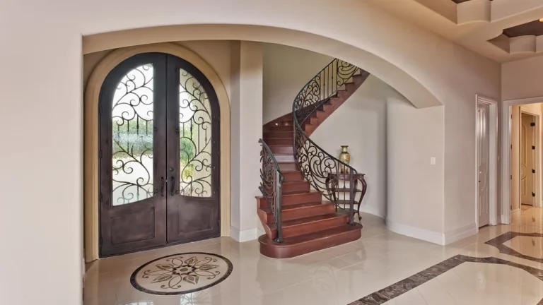 Foyer with arched wrought-iron and glass double doors, a curved staircase with iron railing and a marble floor medallion