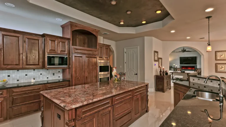 Kitchen with alder cabinetry, a granite island, built-in microwave and wall ovens under a dark tray ceiling, open to the family room