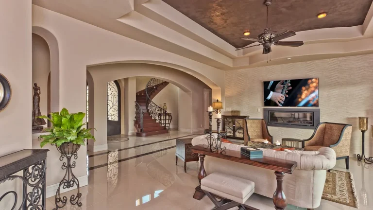 Living room with a linear fireplace and TV wall, tufted seating and an arched view to the curved staircase