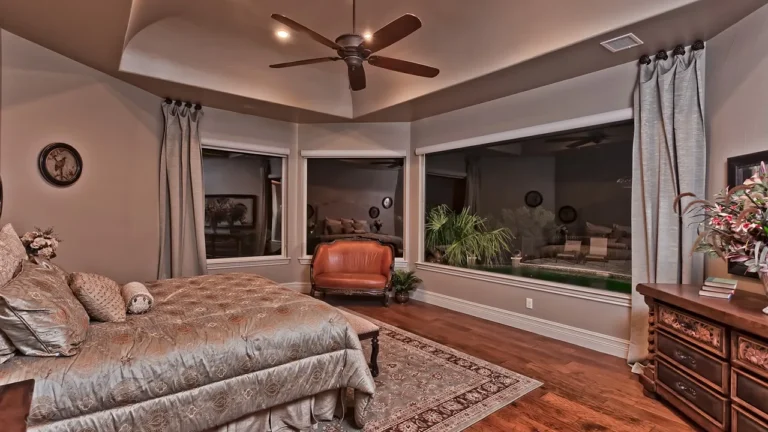 Primary bedroom with a tray ceiling, ceiling fan, hardwood floors and a sitting nook with windows to the patio