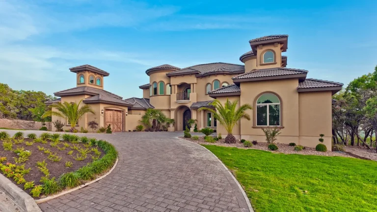 Mediterranean-style custom home with stucco towers, a tile roof, arched windows and a curved paver driveway lined with palms