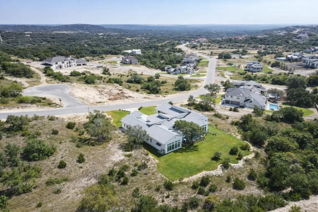 Aerial view of a modern custom home on a large lot in a growing Texas Hill Country community with winding streets