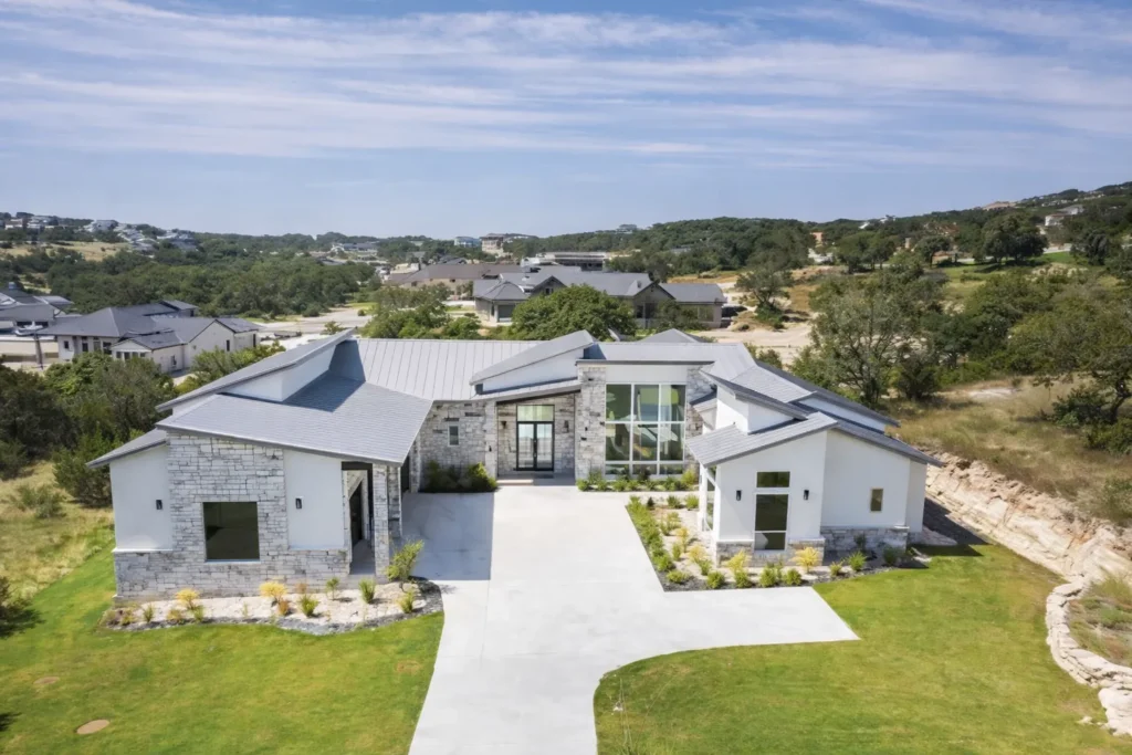 Aerial view of a single-story modern custom home with limestone, white stucco, a metal roof and a two-story glass entry