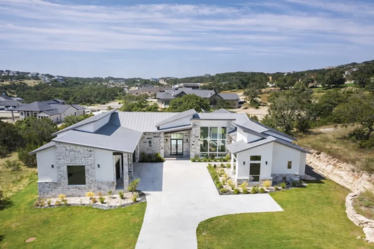 Aerial view of a single-story modern custom home with limestone, white stucco, a metal roof and a two-story glass entry
