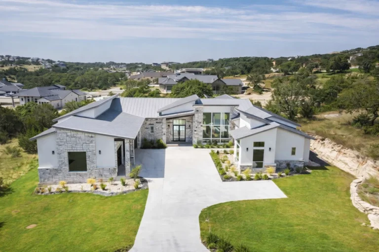 Elevated front view of a single-story modern custom home with a limestone facade, glass entry and curved driveway