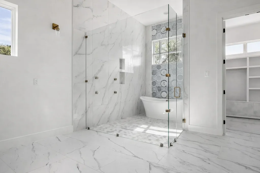 Spa bath wet room with frameless glass, a freestanding tub, marble-look porcelain and brushed brass fixtures