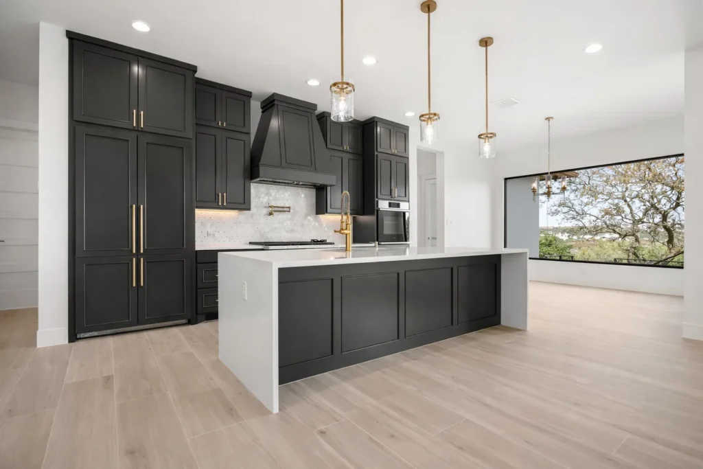 Modern kitchen with black shaker cabinets, a white waterfall quartz island, brass pendants and a picture window to the oaks
