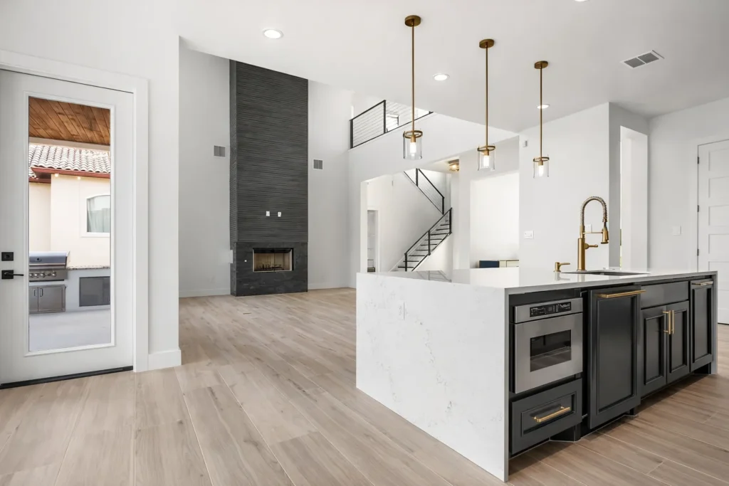 Kitchen with a waterfall quartz island, black cabinets and brass faucet beside a two-story tile fireplace and outdoor kitchen door