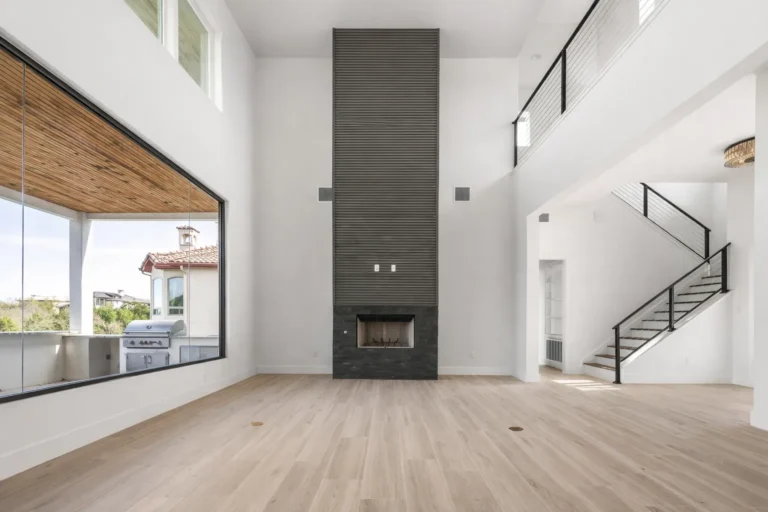 Two-story living room with a charcoal tile fireplace, floating staircase and wall of glass opening to an outdoor kitchen