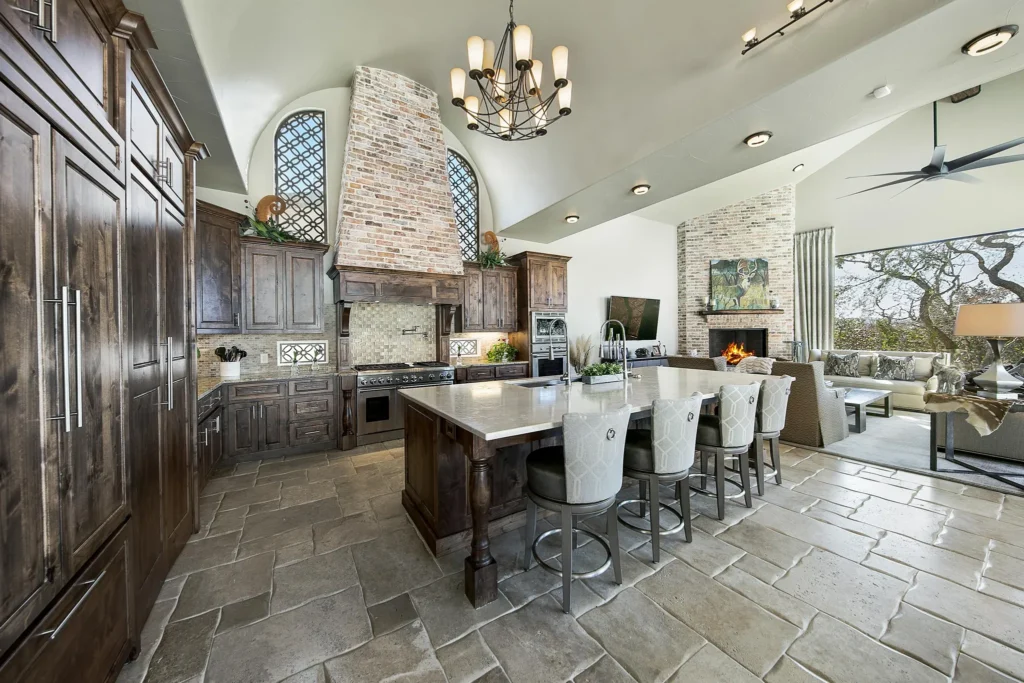 Old-world custom kitchen with knotty alder cabinetry, a brick range hood, wrought-iron chandelier and island seating open to a fireplace family room